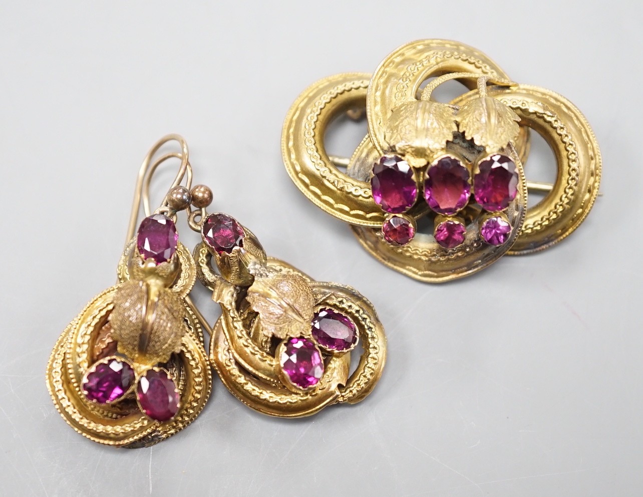 A Victorian yellow metal, oval and round cut garnet set demi parure, comprising a scroll work brooch and pair of matching earrings(a.f.), brooch, 38mm, gross weight 14 grams.